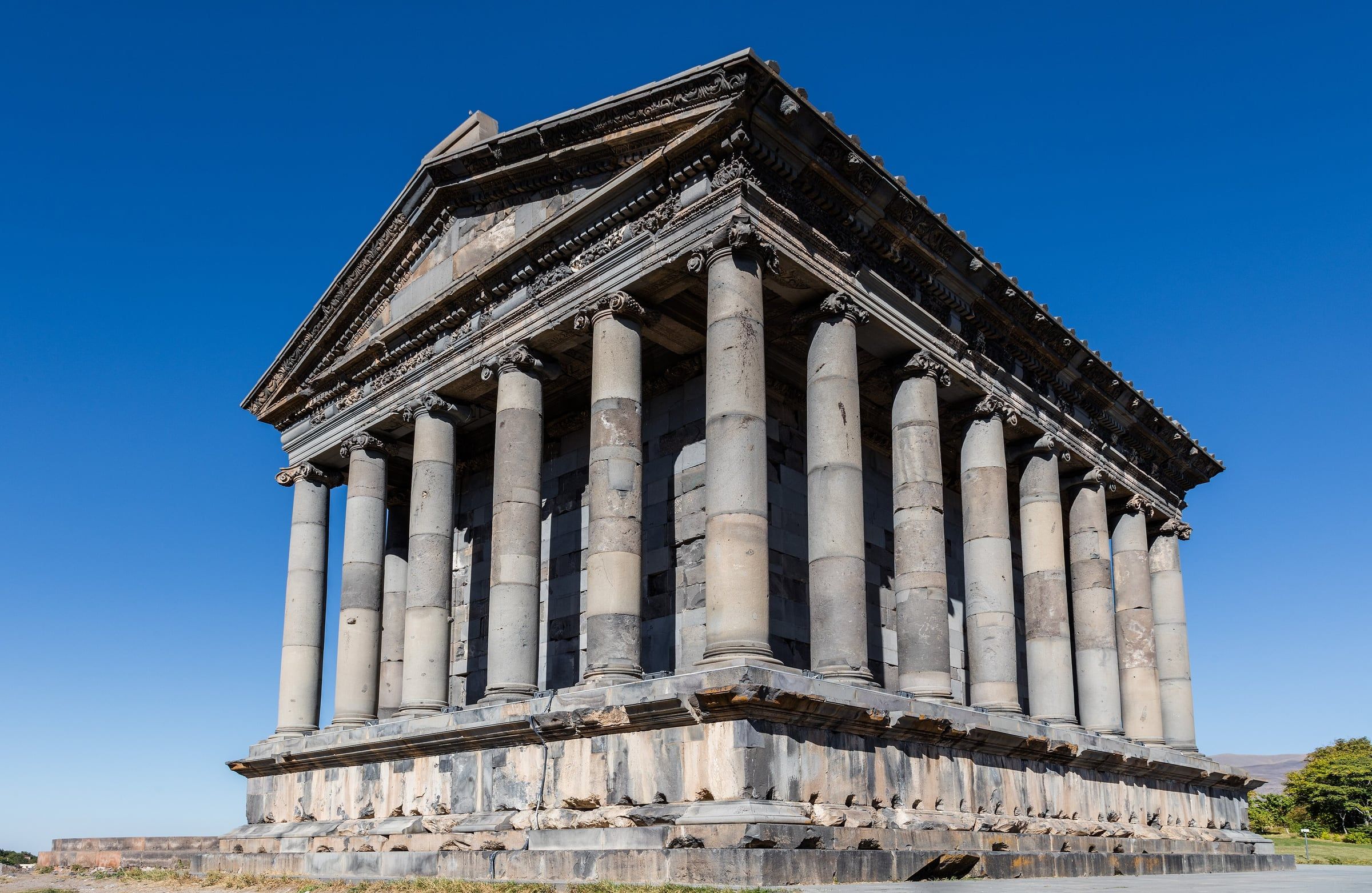 The colonnaded stone temple at Garni stands whole under a clear blue sky, seen from a low angle.